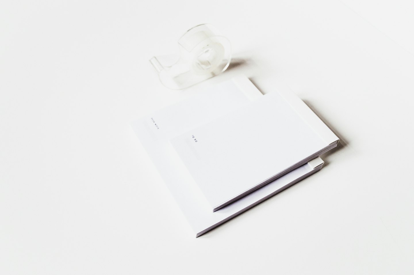 A stack of white notebooks and a tape dispenser.